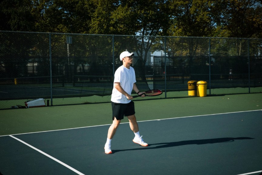 Matt walking across an outdoor tennis court with racket in hand